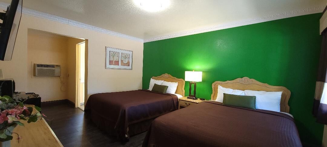 Ein Hotelzimmer mit zwei Betten, einem Schreibtisch mit Lampe und einer Wand in Grüntönen.