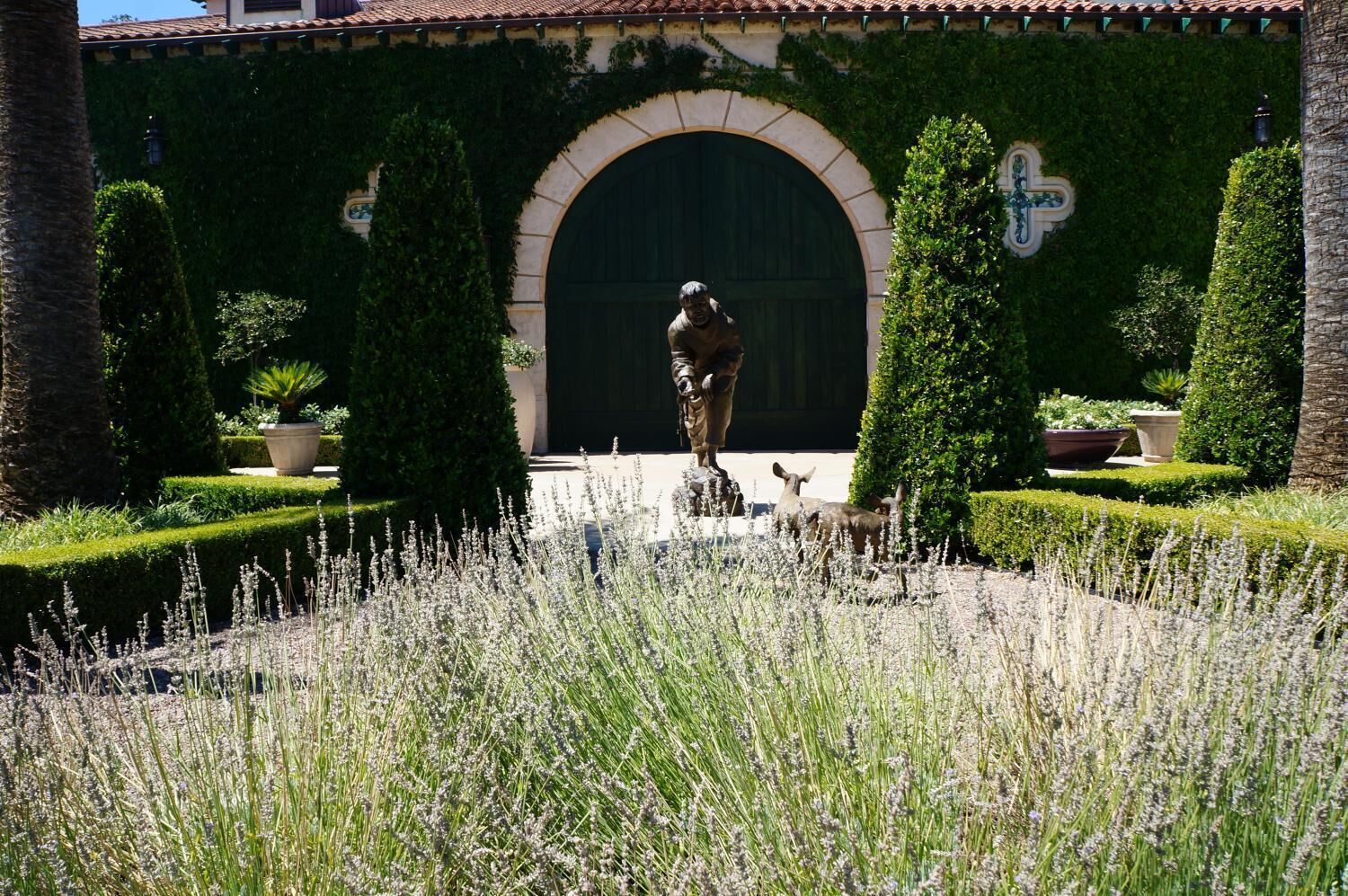 Una estatua de un hombre en un jardín con un amplio arco de entrada y setos bien cuidados.