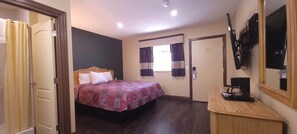 A hotel room with a bed, a desk with a coffee maker, a TV on the wall, and a window with curtains.