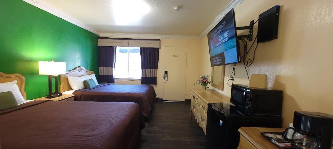 Habitación de hotel con dos camas, televisión, escritorio con computadora y ventana con cortinas.
