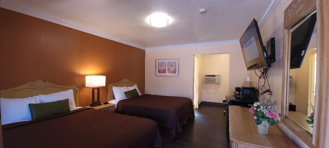 A hotel room with two beds, a desk with a computer, a TV, and a mirror.