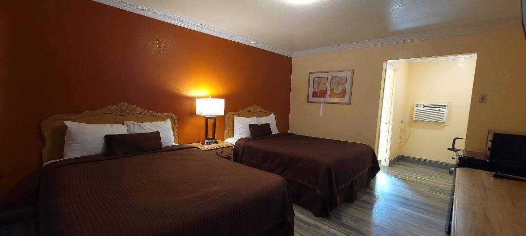 A hotel room with two beds, a nightstand, a lamp, and a desk with a chair.