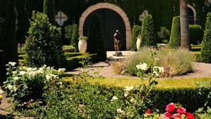 A formal garden with manicured hedges, a statue, and a fountain.