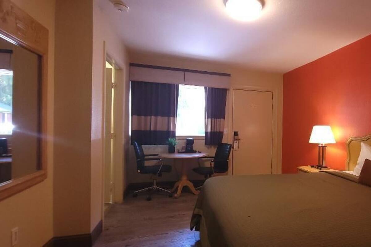 A hotel room with a bed, a desk with a chair, a lamp, and a window with curtains.