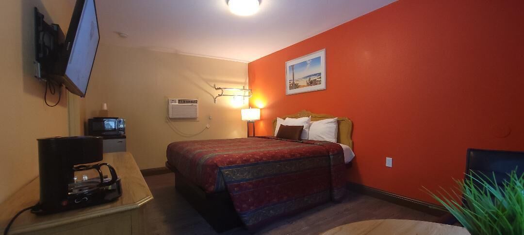 Habitación de hotel con cama, escritorio con computadora, televisor y aire acondicionado instalado en la pared.