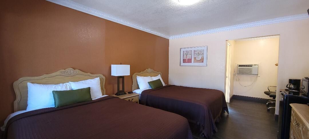 Habitación de hotel con dos camas, un escritorio con lámpara, una silla y un equipo de aire acondicionado.