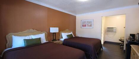 Habitación de hotel con dos camas, un escritorio con lámpara, una silla y un equipo de aire acondicionado.