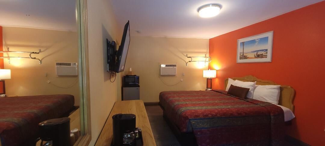 A hotel room with two beds, a desk, a TV, and a painting on the wall.