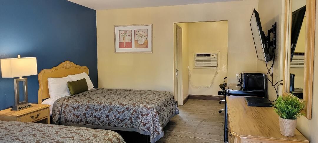 A hotel room with two beds, a desk with a computer, a TV, and a plant.