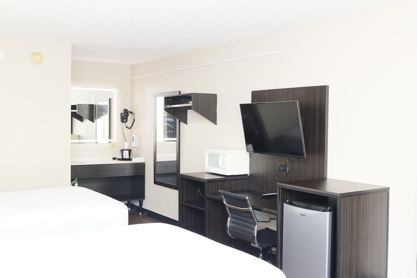 A hotel room with a bed, a desk with a chair, a television, a microwave, and a refrigerator.