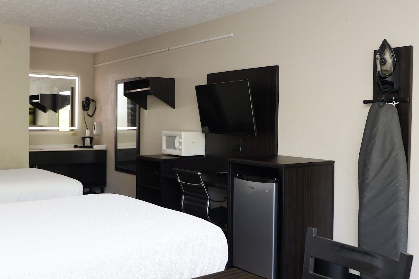 Ein Hotelzimmer mit zwei Betten, einem Schreibtisch, einem Fernseher, einer Mikrowelle und einem Kühlschrank.