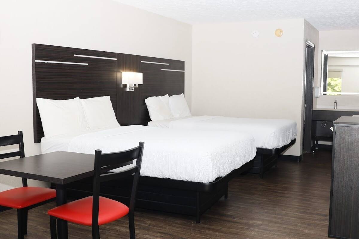 A hotel room with two beds, a desk with a chair, and a small kitchenette.