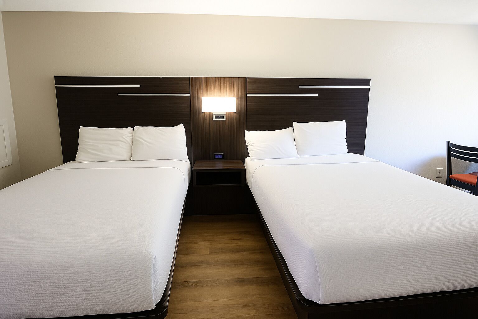 A hotel room with two single beds, a nightstand, a wall-mounted lamp, and a wooden floor.