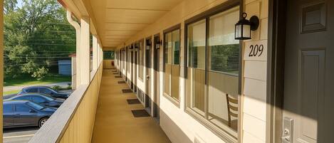 A corridor with doors numbered 209, a covered walkway, and a view of parked cars and greenery outside.
