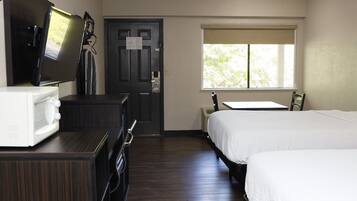 A hotel room with a bed, a desk, a chair, a TV, and a microwave.