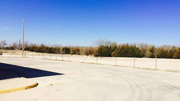 An empty parking lot with a clear sky and a line of trees in the background.