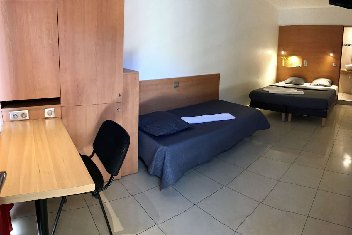 Habitación de hotel compacta con escritorio de madera, una cama individual, una silla y una pequeña zona de kitchenette.