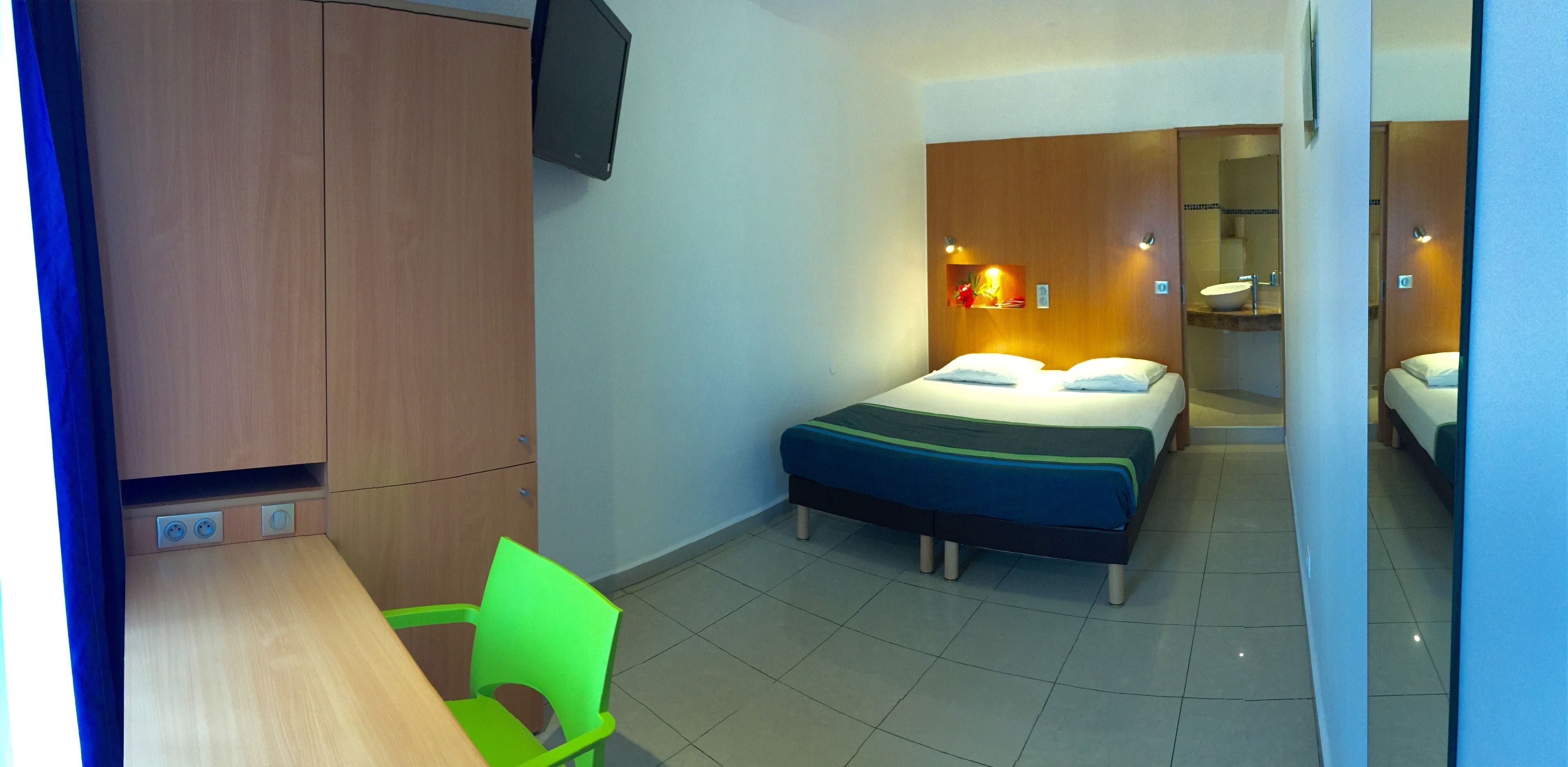 Een hotelkamer met een bed, een bureau, een stoel, een televisie en een badkamer zichtbaar door een geopende deur.