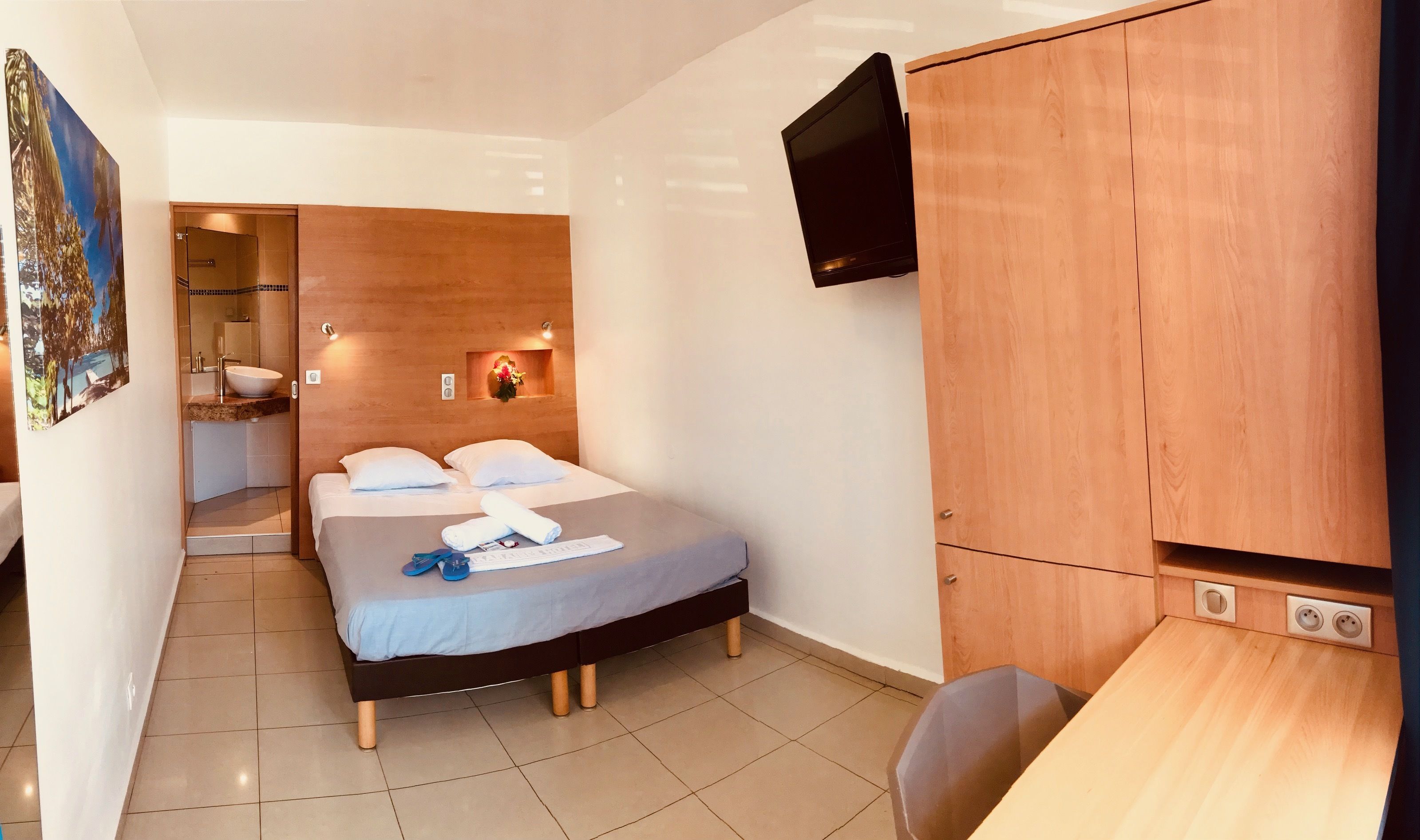 A hotel room with a bed, a desk, a TV, a shower, and a wall-mounted TV.