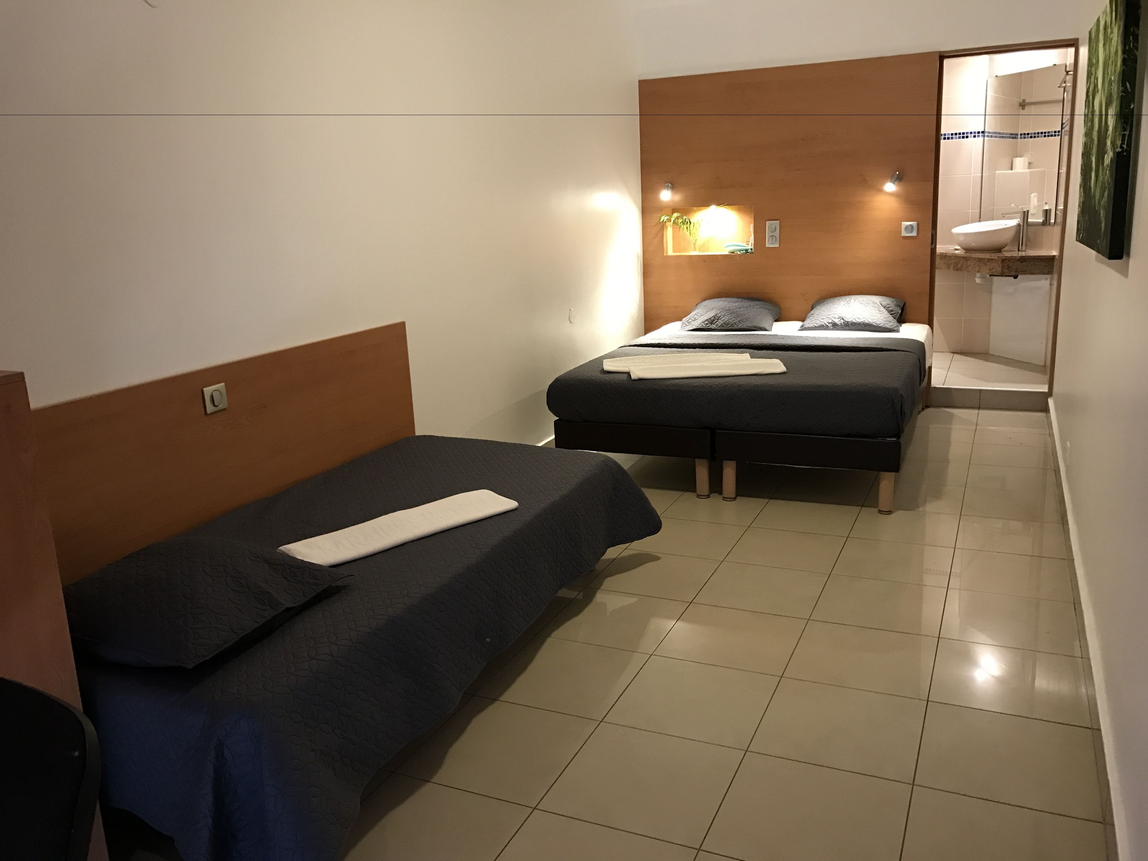 A hotel room with two single beds, a small bathroom with a mirror, and a shower area.
