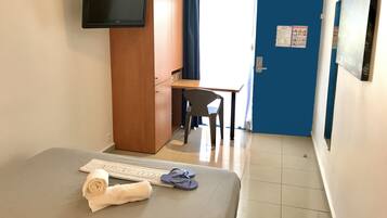 A hotel room with a bed, a desk, a chair, a wardrobe, and a television.