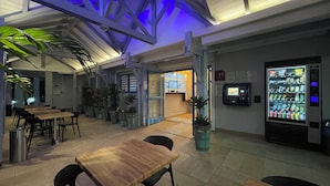 A restaurant with indoor seating, a vending machine, and potted plants. - Karaibes Hotel (Le Gosier)