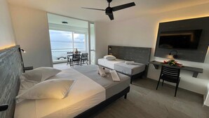 A hotel room with two beds, a ceiling fan, a TV, and a balcony with a table and chairs. - Karaibes Hotel (Le Gosier)