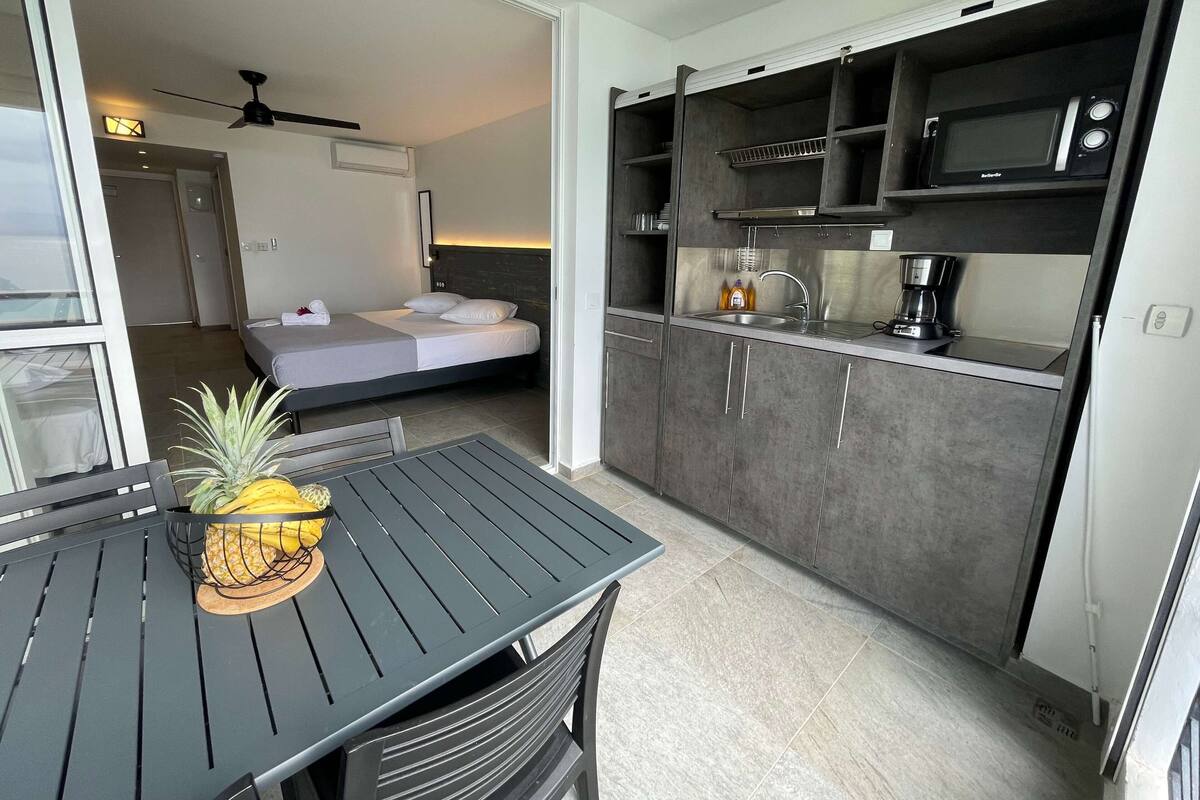 Habitación de hotel pequeña con kitchenette, una cama y zona de comedor con mesa y sillas.
