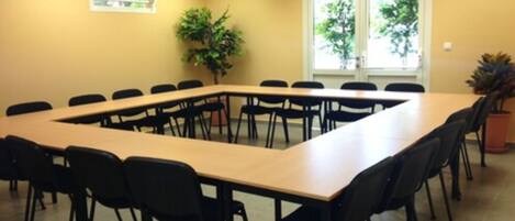 A conference room with a long table and chairs, a potted plant, and windows with a view of trees.