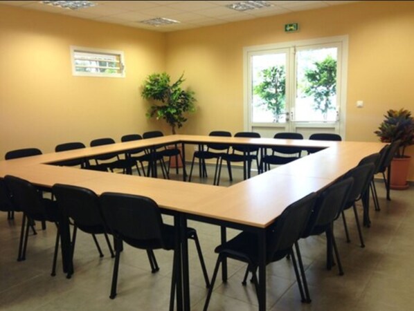 A conference room with a long table and chairs, a potted plant, and windows with a view of trees. - Karaibes Hotel (Le Gosier)