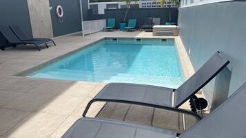 A swimming pool with lounge chairs and a small table.