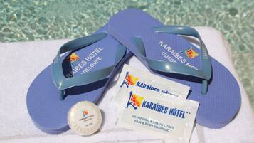 Une paire de tongs, une bouteille de shampoing et un sachet de shampoing pour les cheveux et le corps, le tout provenant de l’hôtel Karāibes.