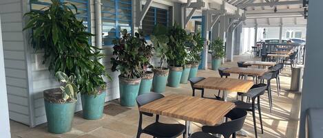 Un área de patio al aire libre con varias mesas y sillas, rodeada de plantas en macetas.