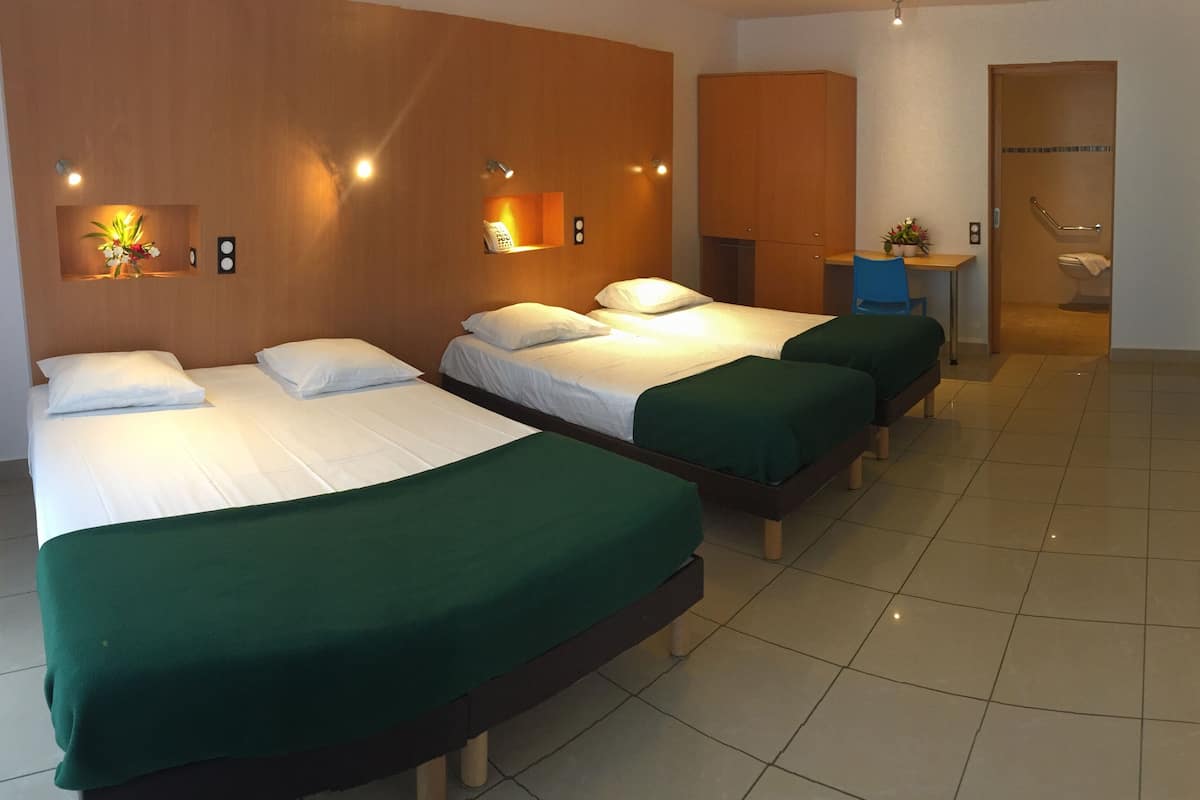 Habitación de hotel con tres camas, un escritorio y un baño.