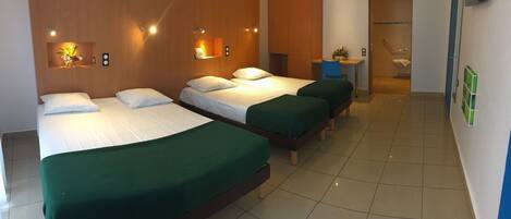 A hotel room with three beds, a desk, and a bathroom.