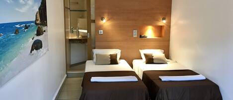 A hotel room with two beds, a wooden headboard, a painting of a beach, and a bathroom visible through an open door.