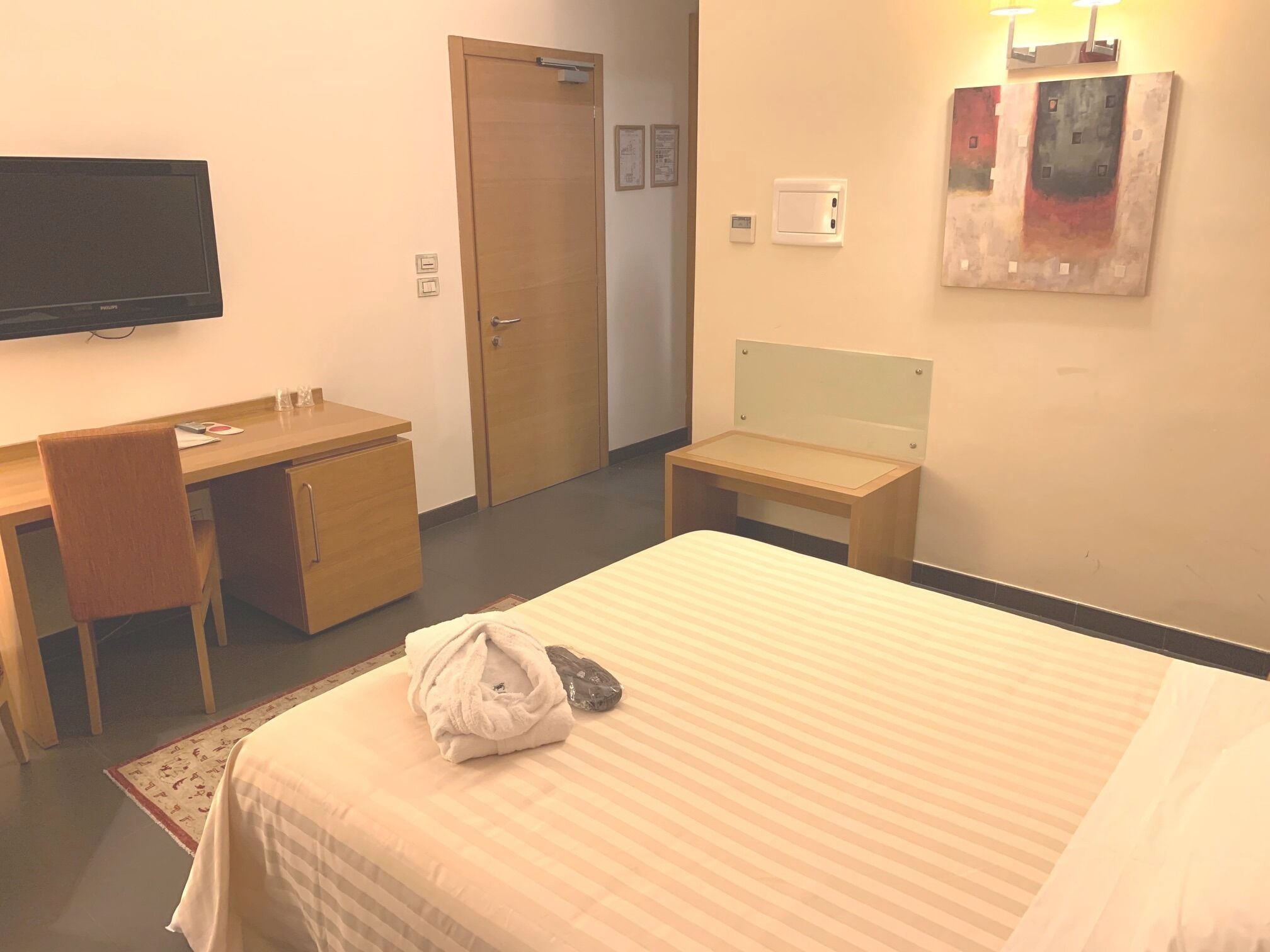 Ein Hotelzimmer mit einem Bett, einem Schreibtisch, einem Stuhl, einem Fernseher, einer Tür und einer Wandleuchte.