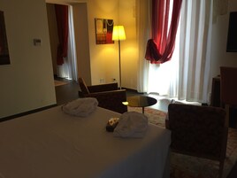 Habitación de hotel con cama, dos sillas, una mesita, una lámpara y un cuadro en la pared.