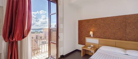 Une chambre d’hôtel avec un lit, une table de chevet, une lampe, une fenêtre avec des rideaux et une vue sur la ville.