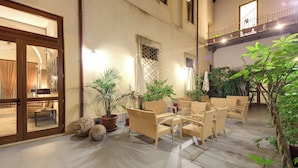 A spacious outdoor seating area with wicker furniture, potted plants, and a view of the building's interior.