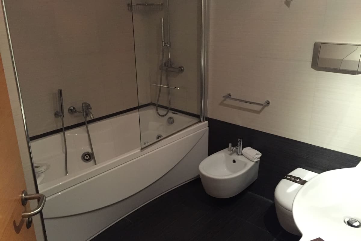 A modern bathroom with a glass-enclosed shower, a white bathtub, a bidet, and a toilet.