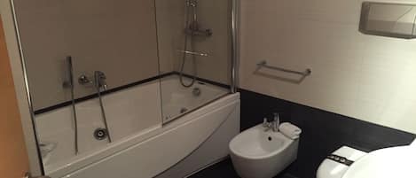 Un baño moderno con ducha envuelta en vidrio, bañera blanca, un bidé y un inodoro.