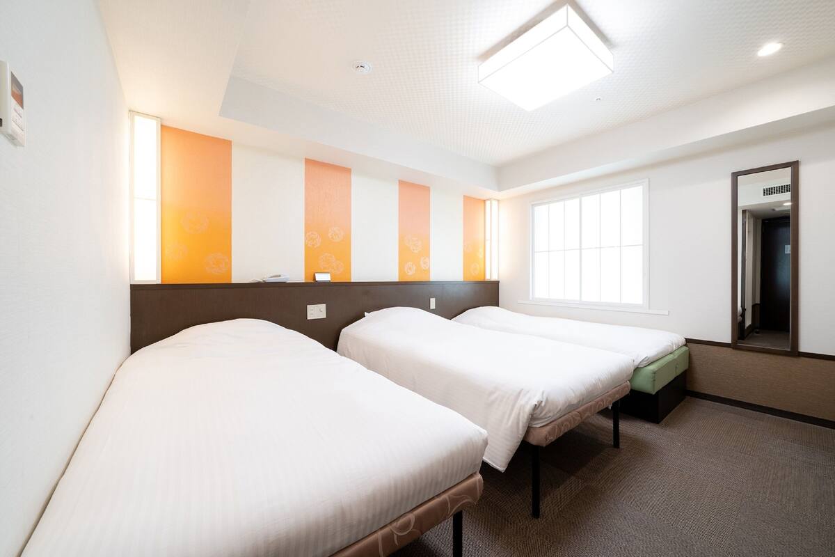 A hotel room with three single beds, a large window, and a mirror on the wall.