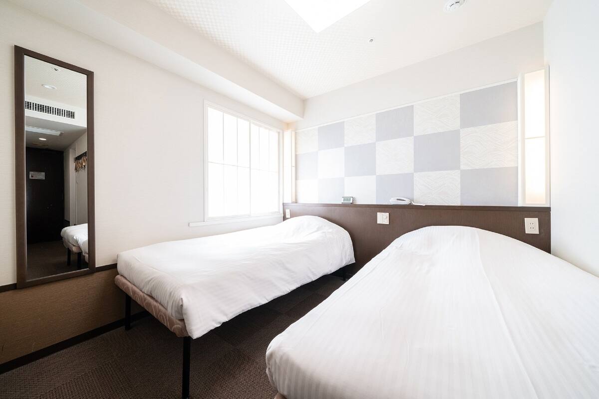 A hotel room with two single beds, a large mirror, a window, and a checkered wall pattern.