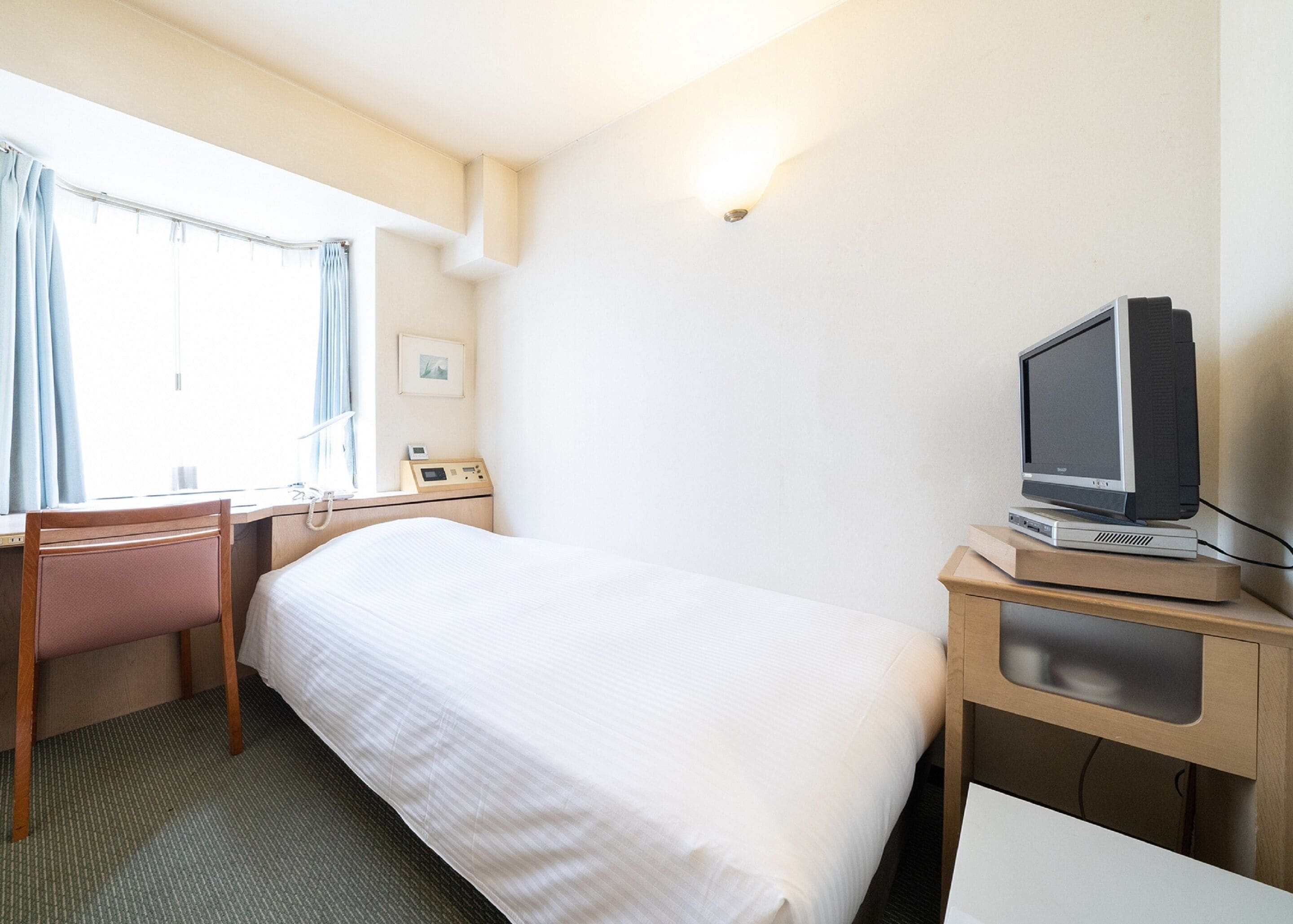 A hotel room with a bed, a desk, a chair, a television, and a window with curtains.