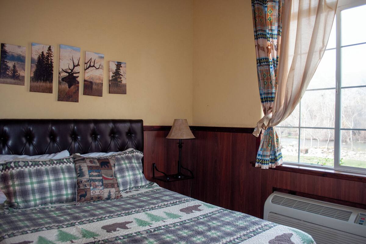 Un dormitorio con una cama, una lámpara de pared, una ventana con cortinas y cuatro cuadros en la pared.