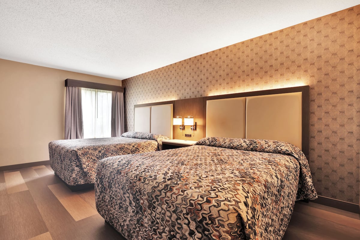 A hotel room with two beds, a large mirror, and a patterned wall.