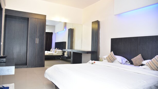 Una habitación de hotel moderna con una cama grande, un armario, una mesita de noche y un espejo.