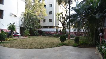 Un patio con suelo empedrado, rodeado de edificios, árboles y una valla blanca.