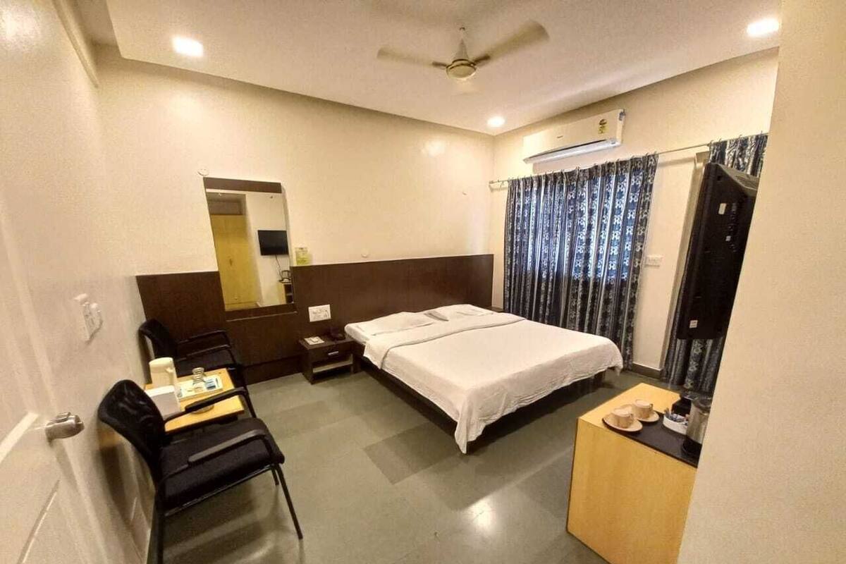 A hotel room with a bed, a desk, a chair, a small table, a mirror, and a ceiling fan.